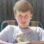 a young lad,15, with light brown hair sits and looks into the camera.