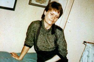 picture of a young woman, short auburn hair, sitting on a bed.