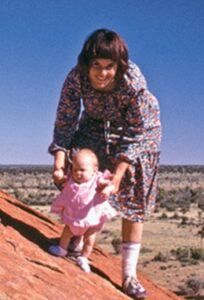 a lady hold a baby as it stands on its own feet